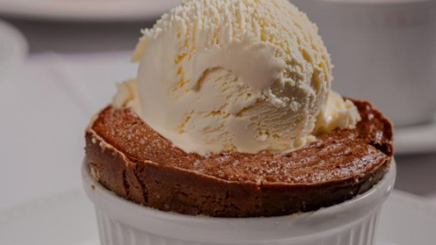 Postre de chocolate horneado, servido en un recipiente individual y acompañado de una bola de helado de vainilla.