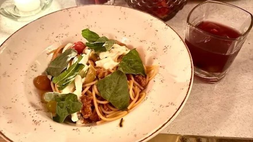Pasta servida con tomates, queso fresco y hojas verdes, acompañada de una bebida.