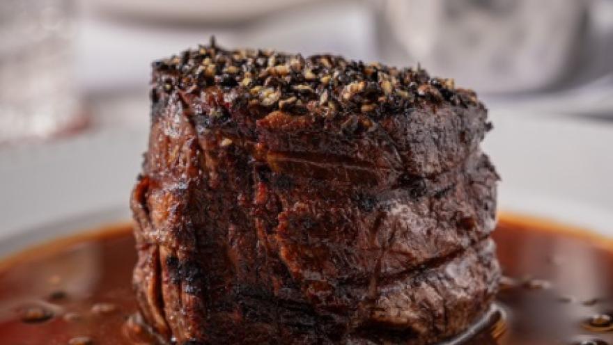 Corte de carne de res a la parrilla, servido sobre una salsa oscura y acompañado de especias.