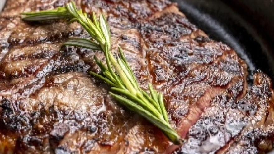 Corte de carne a la parrilla, marcado a fuego y acompañado de una rama de romero fresco.
