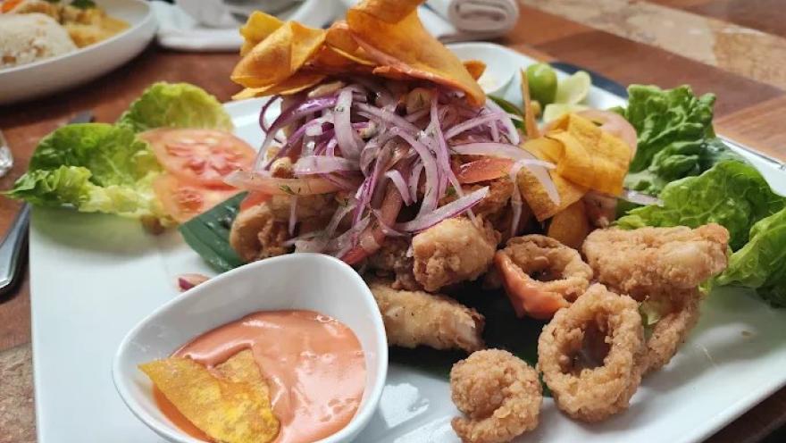 Plato de mariscos fritos acompañado de cebolla morada, lechuga, chips de plátano y salsa cremosa.